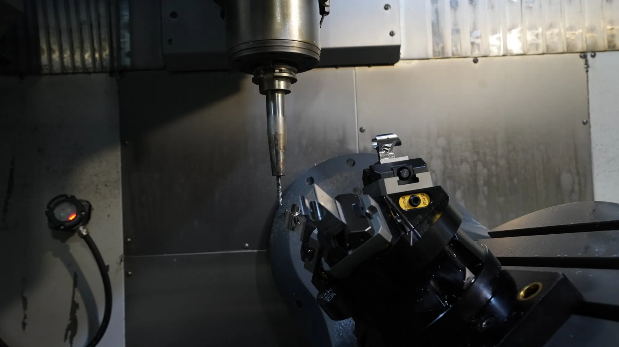 A 5-axis trunnion with a self-centering vise tilted toward the spindle and drill inside a CNC machine at NCX Concepts.