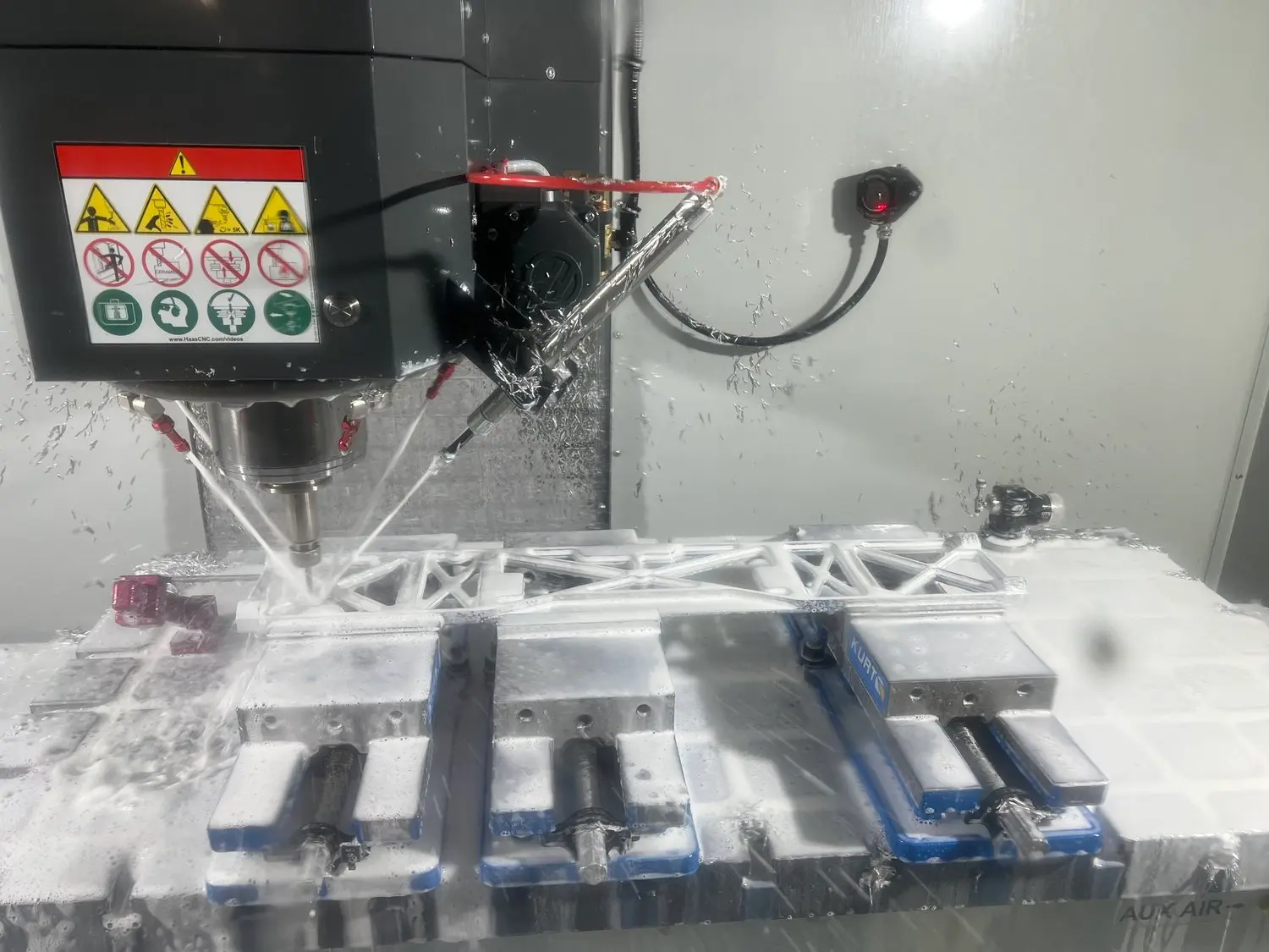 A Haas CNC milling machine cutting a metal part held in vises under flood coolant at NCX Concepts in Charlotte, NC.